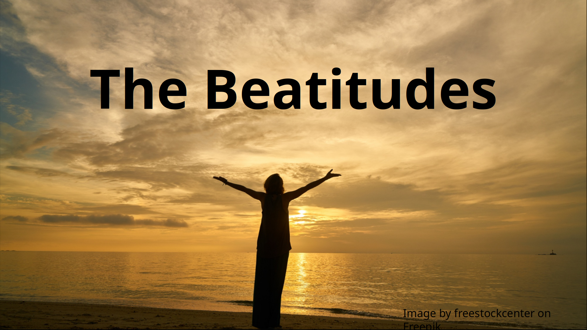 A photograph of a woman with outstretched arms standing on a shore facing the distant sunset.